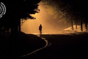Man walking alone along a dark street, casting a long shadow.