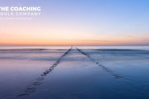 A coastal path revealed in shallow water at sunrise, symbolising clarity and a coaching journey unfolding over time.